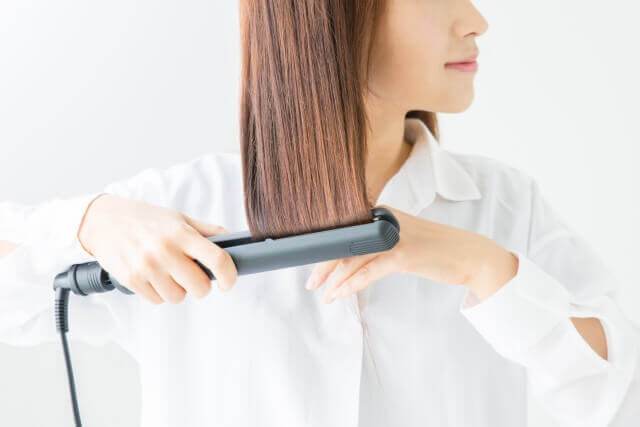 髪にヘアアイロンを当てる女性